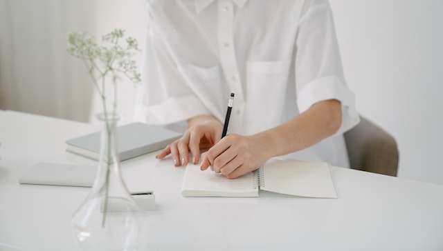 person in all white writing in a notebook with a black pencil